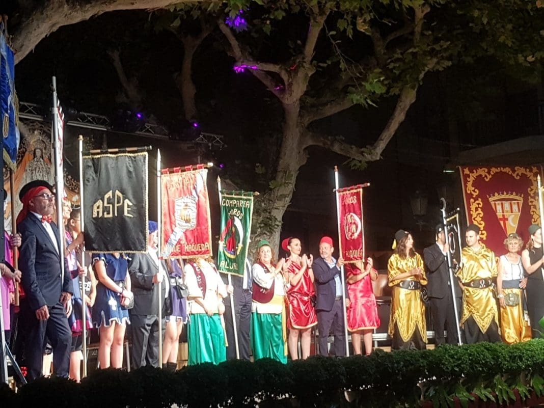 Representantes la fiesta mostrando en el escenario banderines de las comparsas de Moros y Cristianos de Aspe / Alex Ferrer