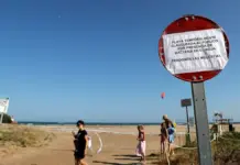 Bañistas junto a una señal de prohibición de bañarse en una playa de Altea