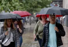 Turistas se protegen de la lluvia mientras pasean en la plaza del Ayuntamiento de València